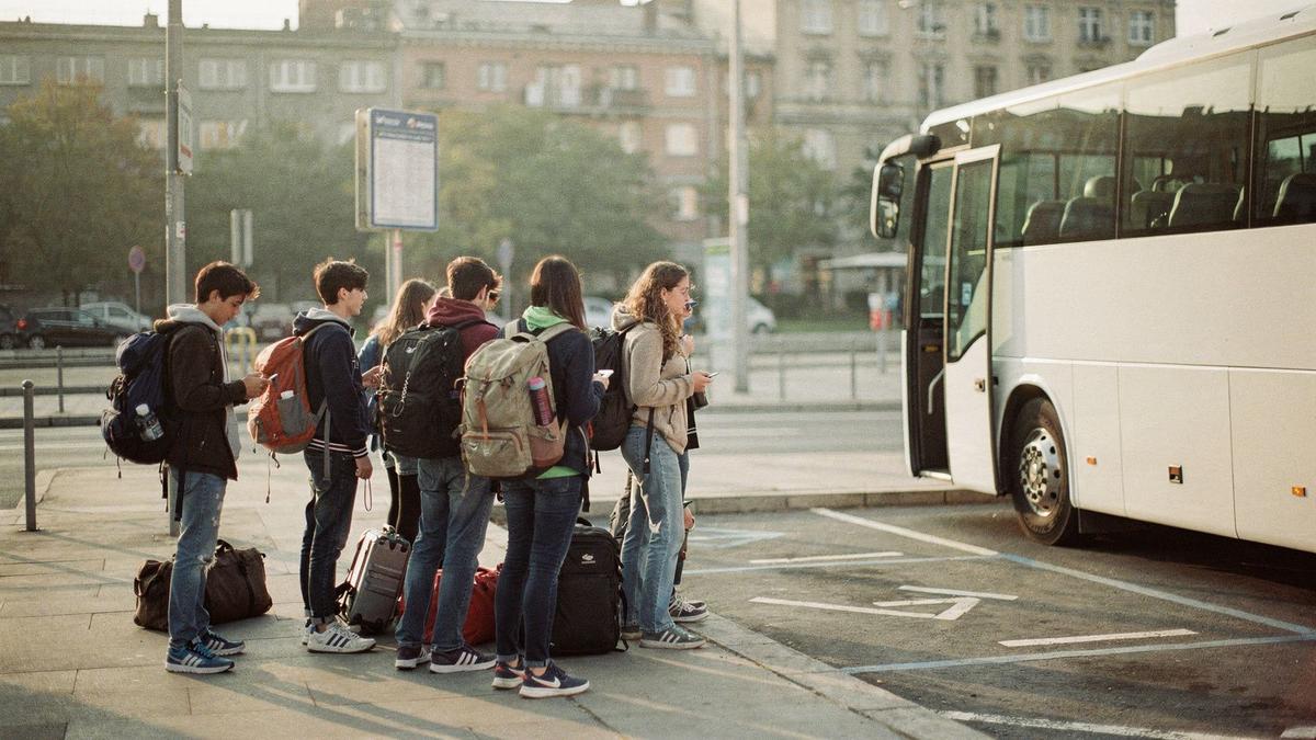 Young travellers with backpacks queuing beside a coach at a city bus bay in the morning